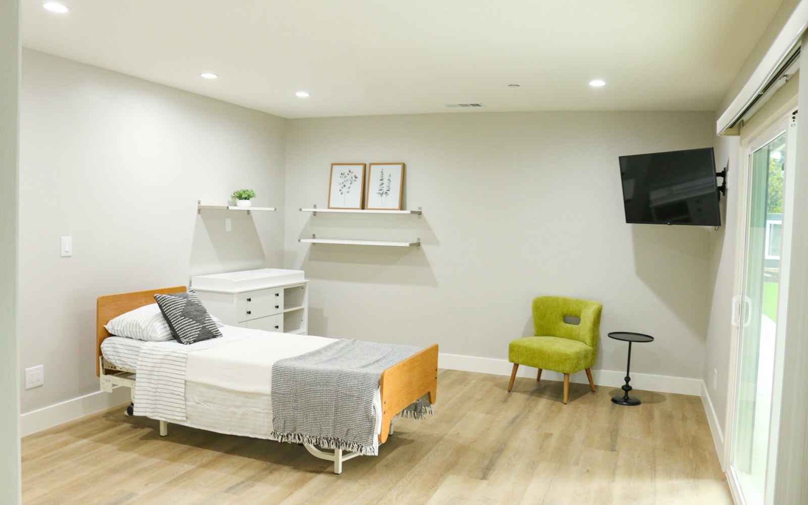 Private care bedroom with an adjustable bed, seating, and a television at a New Start CLHF